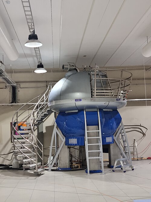 A large NMR spectrometer: a silver domed magnet on a blue cryostat, surrounded by access stairs in a lab.